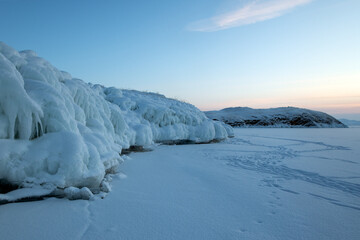 Natural ice formations and frozen splash patterns on a snowy winter landscape on sunrise. Smooth snow surface create a minimalistic arctic scenery with soft pastel sky. Cold seasonal background.