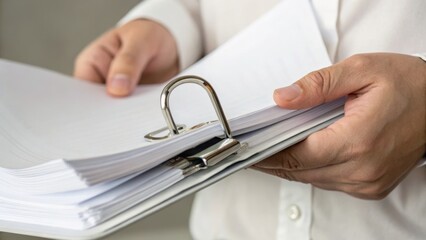 Person holding a thick stack of documents organized with metal ring binders, symbolizing paperwork, organization, and administrative tasks.