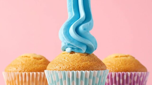 A video food scene showcasing a blue icing being piped onto a cupcake in the foreground with two other cupcakes beside it