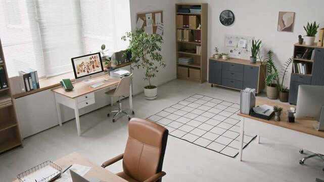 Wide angle shot of office workspace with computer desks standing in room filled with sunlight and decorated with plants, minimalistic open space interior