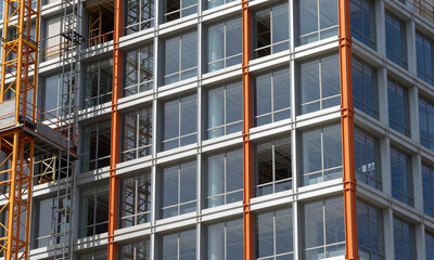 Fototapeta premium view partially constructed modern building exterior features grid orange structural supports amidst glass panels