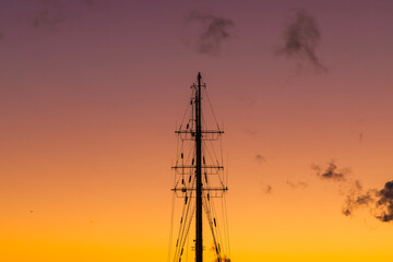Masts of a sailing ship against a colorful sunset sky with clouds