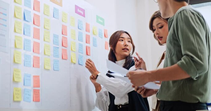 Group of Asian generation z business people work together in home office. Financial team businesspeople brainstorm meeting, use digital tablet and white board presentation. Corporate teamwork concept
