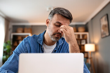 Tired man suffering from headache and eye strain while working on laptop. Healthcare and medicine...