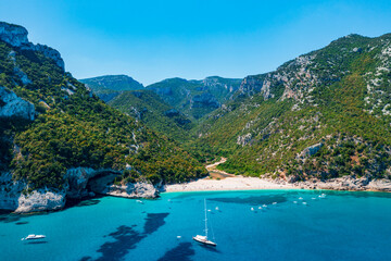 Obraz premium Aerial view of Cala Sisine, beautiful sandy beach with tourquoise water and limestone mountains along the Baunei Coast, Gulf of Orosei, Sardinia, Italy