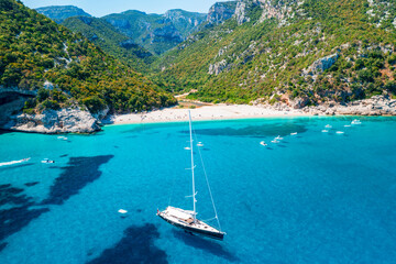 Obraz premium Aerial view of Cala Sisine, beautiful sandy beach with tourquoise water and limestone mountains along the Baunei Coast, Gulf of Orosei, Sardinia, Italy