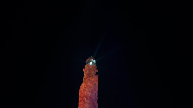 Faro mar&iacute;timo iluminando durante la noche con luz giratoria y cielo oscuro