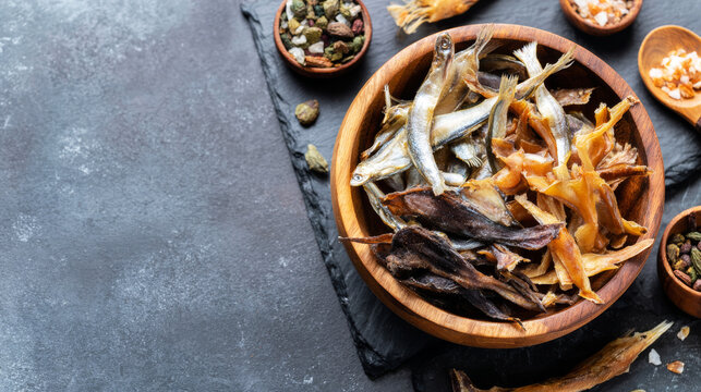 Dried assortment of seafood snacks and small fish in a wooden bowl with traditional seasonings and copy space