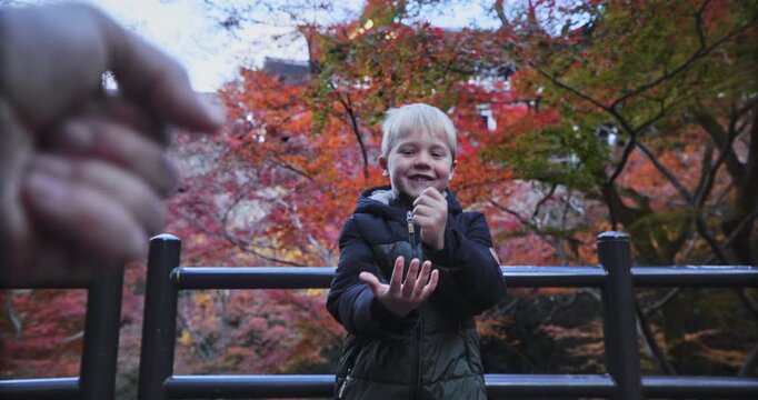 Point of view of man playing rock, paper scissors with little boy in front of autumn trees
