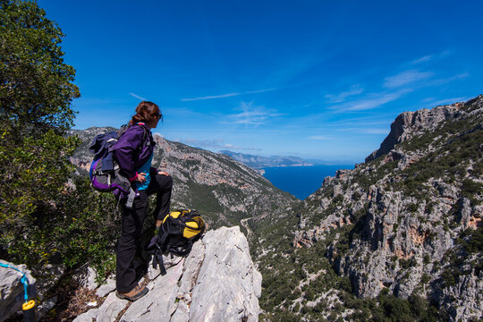 Female trekker overlooking the Mediterranean Sea from the cliffs of Baunei coast, Supramonte, Sardinia, Italy.