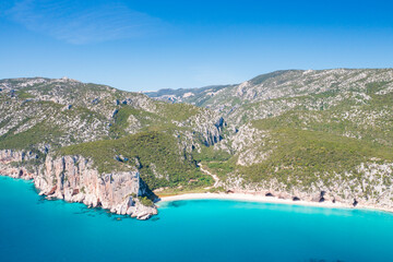 Obraz premium Aerial view of Cala Luna beach on the coast of Baunei and Dorgali, Sardinia, Italy. Turquoise water, white sandy shoreline and dramatic limestone cliffs along the Gulf of Orosei.