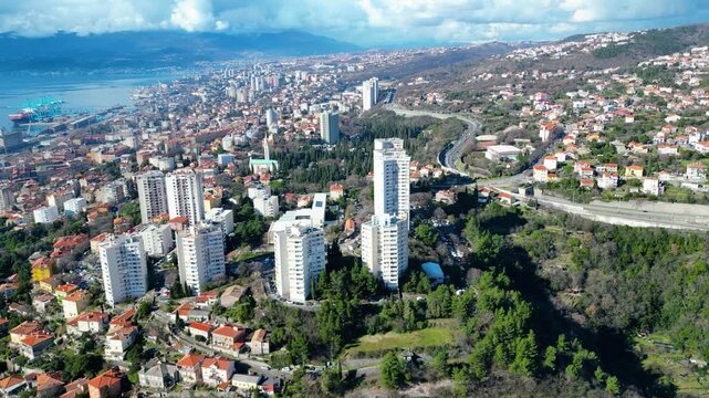 Aerial view of Rijeka, Croatia, showcasing its vibrant port, urban sprawl, and lush hillsides under a bright midday sky.