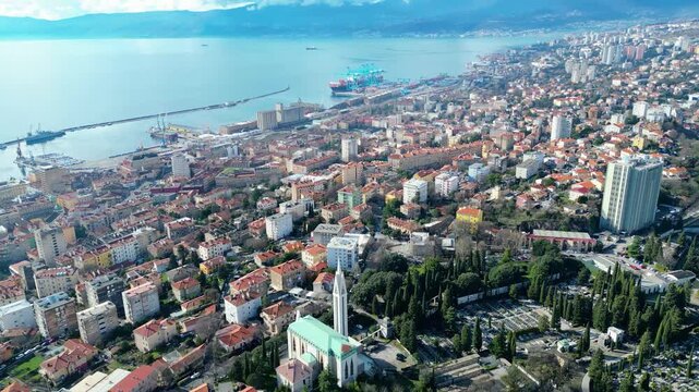 An expansive aerial view of Rijeka, Croatia, showcasing its vibrant port, historic architecture, and the iconic Church of Our Lady of Lourdes under a clear sky.