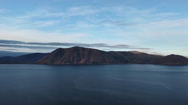 Mountain coast and wide bay near Provideniya in Chukotka. The drone makes a slow pan across the water toward Bering Strait. Blue summer evening tones create a cinematic mood