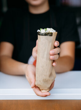 Hand holding sushi burrito in paper wrap, takeaway street food close up