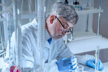 Experienced senior scientist working in a modern laboratory, carefully analyzing chemical samples among glass flasks and test tubes. © TSViPhoto