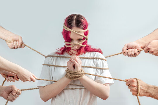 Teen girl tied with rope and pulled from different sides by hands, concept of domestic abuse, hostage and violence threat, loss of autonomy, fear, trauma and mental health crisis.