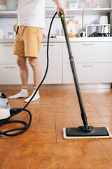 Fototapeta premium Person using steam cleaner device to sanitize and deep clean kitchen floor, performing domestic chore for efficient home sanitation and hygiene. Concept of maintenance modern home appliance.