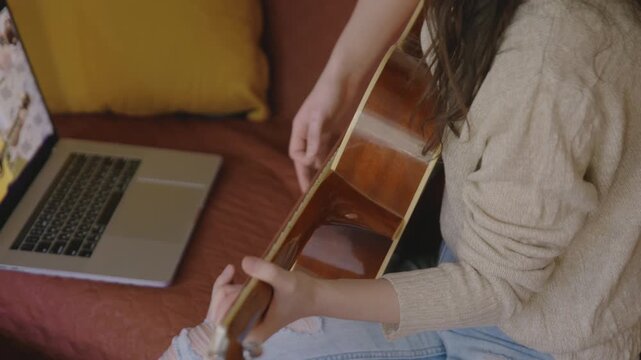 Young asian woman playing guitar at home. Stay home, solo activity Pretty girl watching online lesson and practising music. Aspiring musician learning to play musical instrument using laptop.