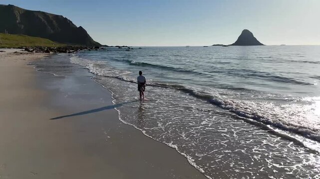 forward drone flight over sandy beach onVesteralen, Vester&aring;len islands. Caucasian man walking with bare feet in the see. Drone view, man enjoying summer in Norway. Tourist walking of beach. Outdoors.
