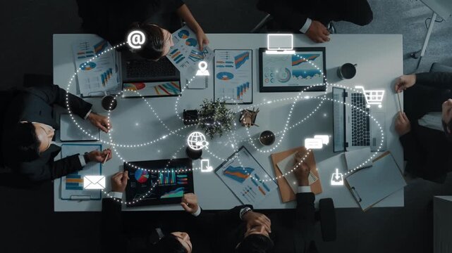 A high-angle view of a business meeting in a modern office featuring digital connectivity, data charts, and collaborative discussions among team members. Raster