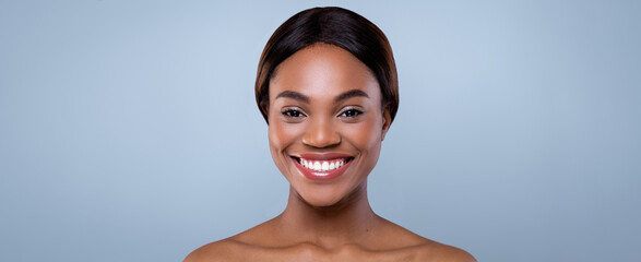A woman stands in front of a smooth background, smiling widely and showing her teeth. Her expression conveys happiness. This moment captures a sense of warmth and positivity in her demeanor. © Prostock-studio