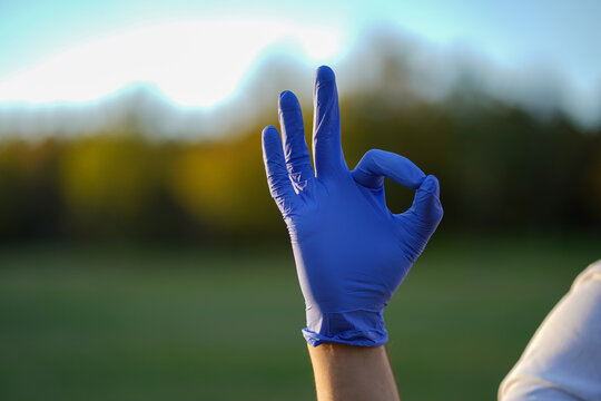 Blue medical glove hand showing OK sign outdoors, healthcare approval gesture