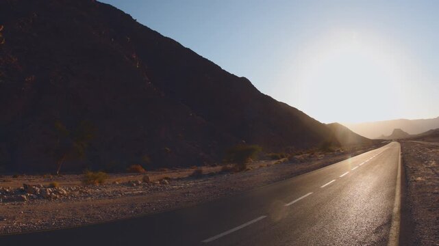 An asphalt road at dawn in the desert. The sun rises, bathing the endless desert expanse in golden light.