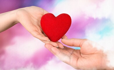 Fototapeta premium People hands holding red heart on pink background.