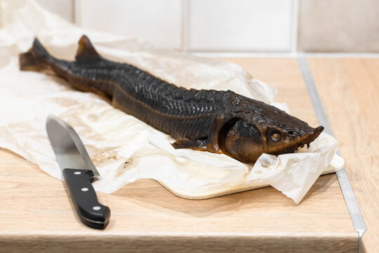 A whole hot smoked sterlet fish and chef knife lay on crumpled parchment