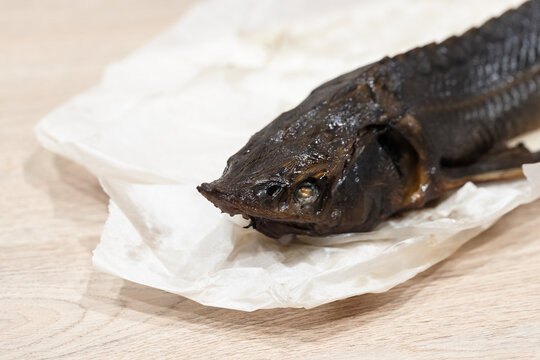 A head of whole hot smoked sterlet fish lying on white parchment