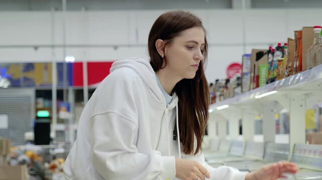 Young woman examines frozen meals in a supermarket, comparing different options in the freezer aisle while deciding on her next meal choice