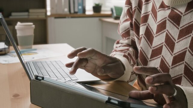 Close up on hands of mature American male office administrator wearing silver ring typing on digital tablet then using touchpad on laptop while managing multiple tasks in modern office workspace