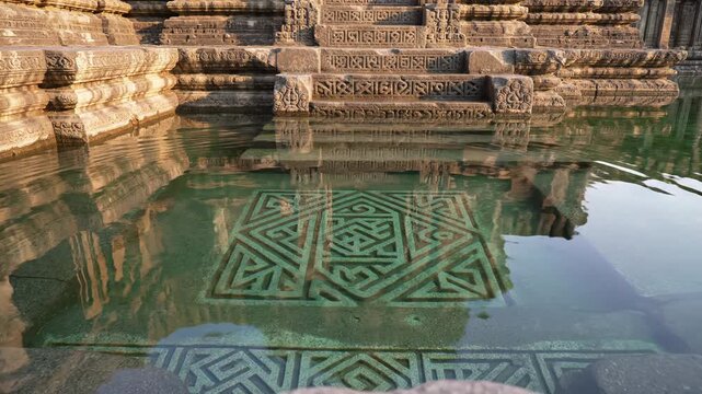Ancient Stone Carvings Reflected in Clear Water at Historic Temple Steps Illuminated by Warm Sunlight Creating Geometric Patterns in the Submerged Architecture of Konark Sun Temple India