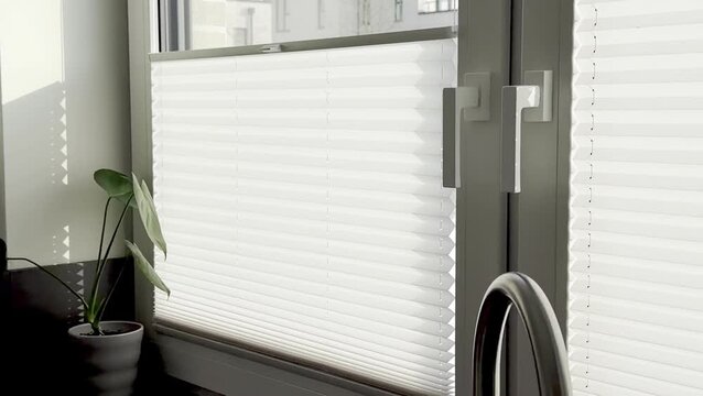 Modern kitchen window with white pleated blinds gradually adjusting to let in natural light