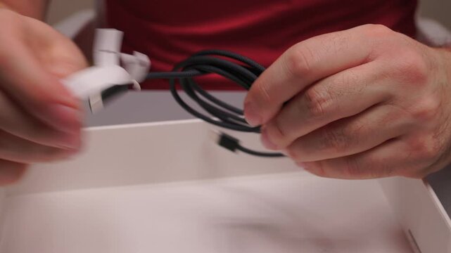 Hands unpack accessory. Studio shot focusing on consumer tech accessory unveiling. Detailed view of hands handling braided charging cord and metal connector in studio setting