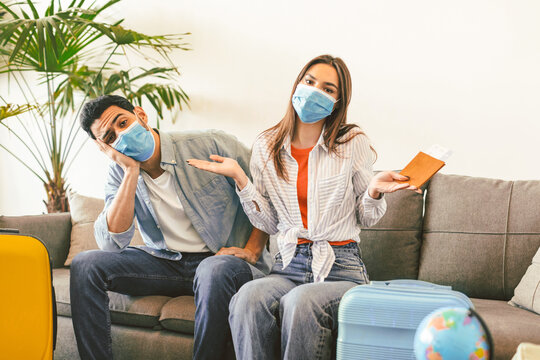Upset tourists couple after tour cancellation sitting on sofa with paked suitcases and travel tickets. Vacation problem and restrictions for tourists during epidemic