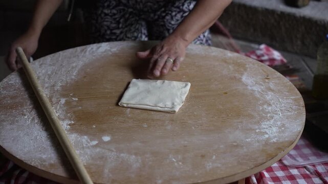 Person rolling out dough on wooden table for bread preparation