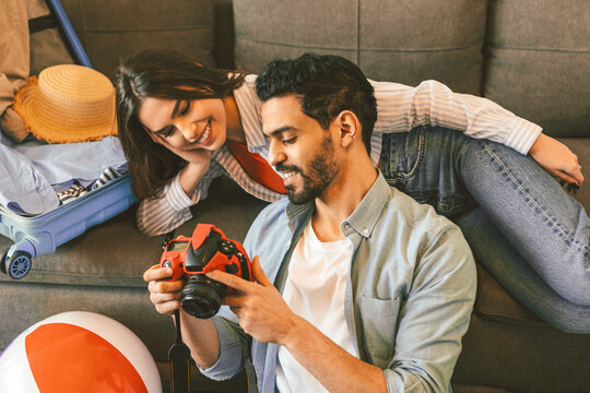 Loving spouses prerating for vacation, packing suitcase and using camera for watching photos in trip. Happy couple preparing for travel abroad, sitting at home with buggage nearby