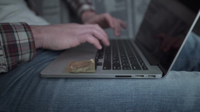 Man using laptop for online dating with a condom nearby. Concept of safe sex and protection during casual encounters. Responsible behavior and health awareness in digital age hookup culture.