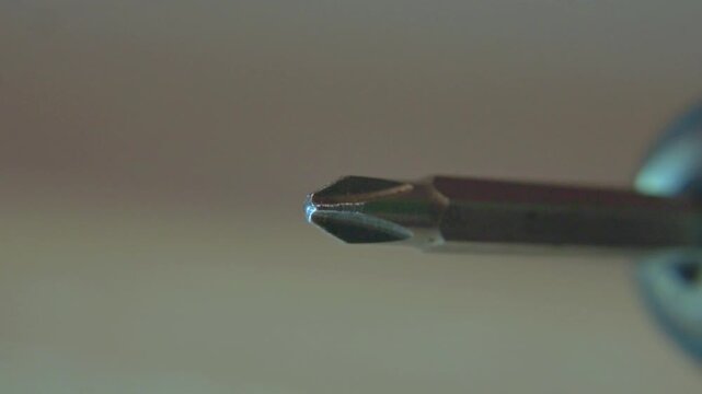 macro close up of metal crosshead phillips screwdriver bit spinning in slow motion against blurred neutral background showing industrial precision and metallic texture of rotating tool