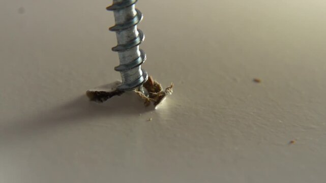 macro close up of metal furniture screw being ripped out of white wooden surface with wood chips flying in slow motion showing furniture breakage and material failure