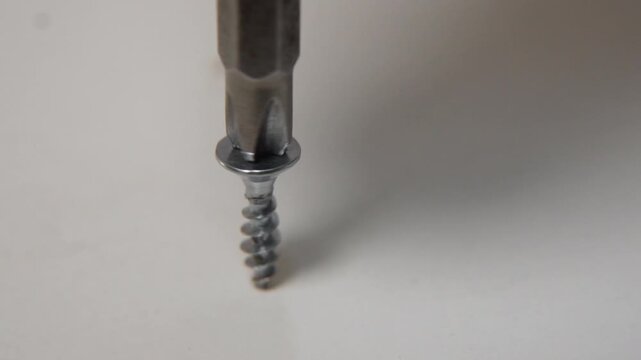 macro close up of steel screw being driven into wooden furniture surface with phillips bit in slow motion showing craftsmanship during home repair or construction work
