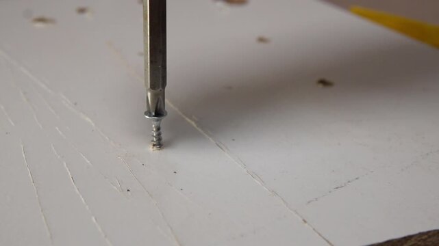  macro close up of steel screw being driven into wooden furniture surface with phillips bit in slow motion showing craftsmanship during home repair or construction work