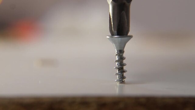 macro close up of steel screw being driven into wooden furniture surface with phillips bit in slow motion showing craftsmanship during home repair or construction work