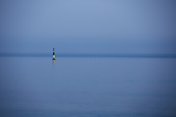 Fototapeta premium Lone navigation buoy in calm blue sea under hazy sky