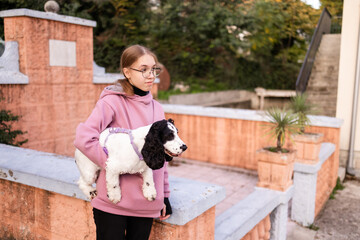 Teenage blonde Slavic girl carrying her Russian spaniel dog along a stone wall in Montenegro
