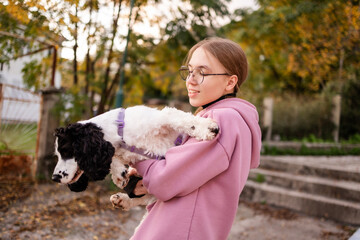 Teenage blonde Slavic girl carrying her Russian spaniel dog along a stone wall in Montenegro