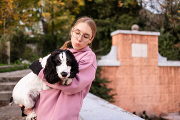 Teenage blonde Slavic girl carrying her Russian spaniel dog along a stone wall in Montenegro