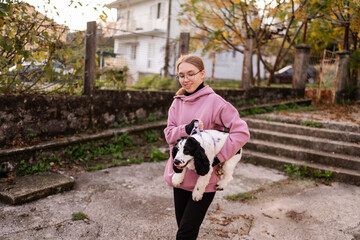 Teenage blonde Slavic girl carrying her Russian spaniel dog along a stone wall in Montenegro